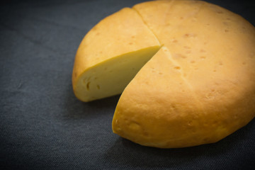 Head of yellow smoked cheese on a dark background