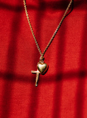 cross and heart on chain in front of shadowy red background - 214272042