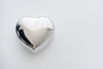 old casket in the shape of a heart on a white leather background. Silver box in the shape of a...