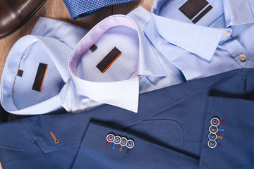 set of classic mens clothes - blue suit, shirts, brown shoes, belt and tie on wooden background.