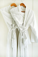 Two white coats hanging on the door. Hotel dressing gowns on the door hanger.