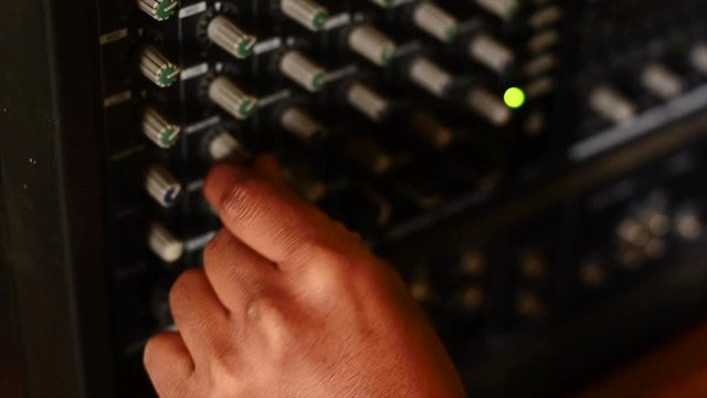 Hands turning knobs to electric amplifier. 