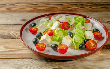 Greek salad with feta cheese, cherry tomatoes and olives in a round plate on a wooden background. Summer menu.