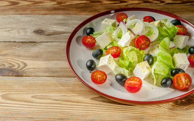 Greek salad with feta cheese, cherry tomatoes and olives in a round plate on a wooden background. Summer menu.