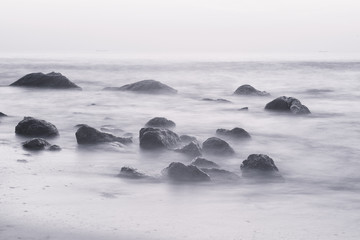 Summer seasonal natural vacation background. Romantic morning at sea. Big boulders sticking out from smooth wavy sea. Long exposure. Black and white