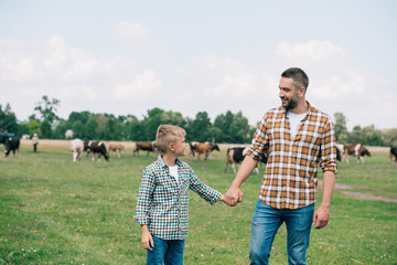 happy father and son holding hands and smiling each other at farm