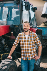 handsome middle aged farmer standing near tractor and smiling at camera