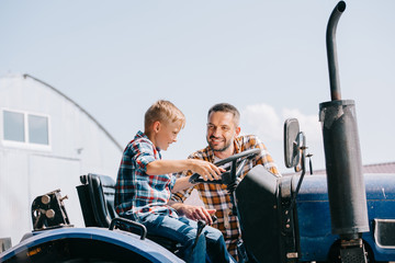 happy father looking at smiling son sitting in tractor on farm © LIGHTFIELD STUDIOS