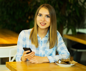 Young beautiful woman is drinking coffee and reading the morning news by the mobile phone internet connection while sitting in a cozy coffee shop in the morning.