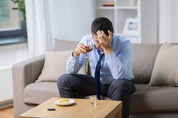 alcoholism, alcohol addiction and people concept - male alcoholic drinking brandy and smoking cigarette at home