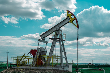 Oil pump tower in the field with green grass with blue cloudy sky