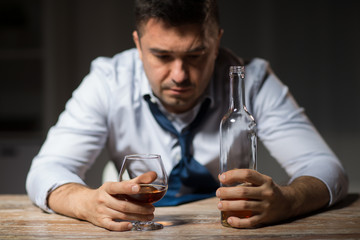alcoholism, alcohol addiction and people concept - male alcoholic with bottle drinking brandy at table at night