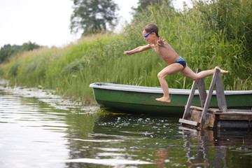 Fototapeta na wymiar A boy jumping into the water in flight against the backdrop of a rural landscape.