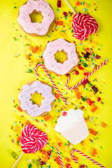 Sweets creative lay out, dessert concept with lollipops, jellies, candy, cookies donuts and cupcakes, bright yellow background top view copy space