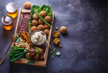 Pastrami, falafel, babagahanoush, veggies and beer in a wooden box, copyspace.