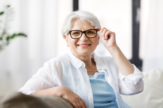 vision, age and people concept - portrait of happy senior woman in glasses sittin on sofa at home