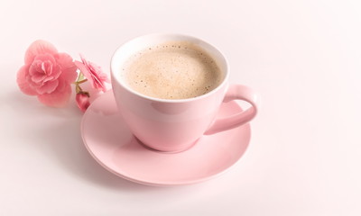 A cup of cappuccino coffee in a pink cup and a pink flower on a light background. 