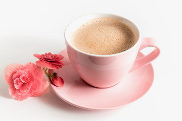 A cup of cappuccino coffee in a pink cup and a pink flower on a light background. 