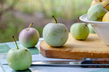 Apples and a knife on a table, on a wooden stand, in a plate on the right.