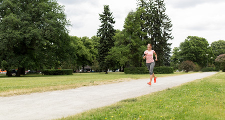 fitness, sport and healthy lifestyle concept - smiling woman with earphones running at park and...