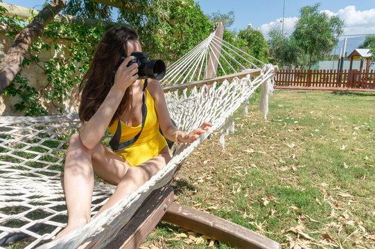 Girl in yellow body sits in a hammock and takes pictures on a SLR camera