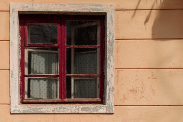 Fototapeta na wymiar Old window in abandoned house with wooden red frame and curtain