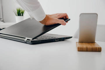 Man, businessman working in the office. The employee closes the laptop, finishing work in the office. A man dressed in a white shirt and a blue tie is working.