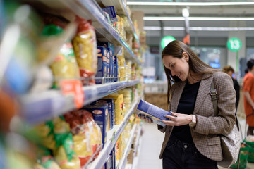 A young woman in the store reads the label of pasta in the package