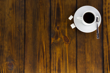 Black coffee with 2 sugars, white cup on a brown wooden table. Top view
