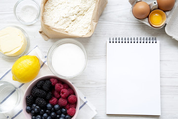 Raw ingredients: berries, eggs, lemon, flour, sugar, salt, water for cooking berry pie with blank notepad, top view. From above, overhead, flat lay. Space for text.