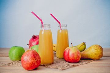 Glass bottle of fruit juice on a wooden table with Apples, pears, pomegranate and banana