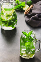Mojito cocktail in mason jar with mint and lime on black stone table. Copy space for text.