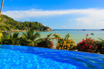 Empty infinite pool by calm sea on sunny day in Thailand. Colorful flowers and palm trees on tropical exotic vacation, summer holidays destination, tourism attraction, paradise concepts