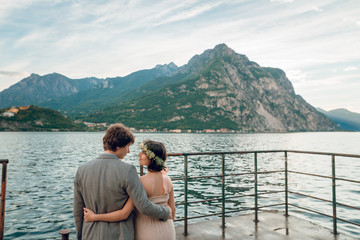 Rear view of young couple standing on the shore with scenic view of lake Como and beautiful mountains on background. Happy family