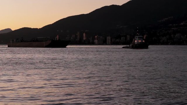 Tugboat Pulling Cargo Ship Across Ocean Harbour At Sunset