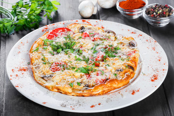 Omelette with slices ham, mushrooms, greens, cheese and tomato on dark wooden background. Hot and healthy breakfast, pizza.