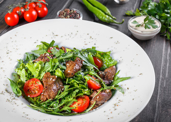 Hot salad with fried liver, cherry tomatoes and mixed greens on dark wooden background. Healthy food. Ingredients on table.