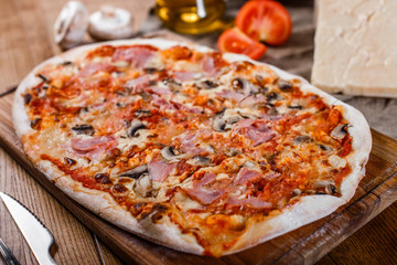 Pizza with ham, cheese, mushrooms and tomato sauce on wooden rustic table. Top view.