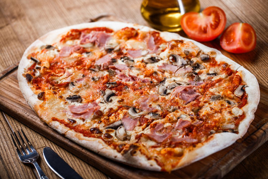 Pizza with ham, cheese, mushrooms and tomato sauce on wooden rustic table. Top view.