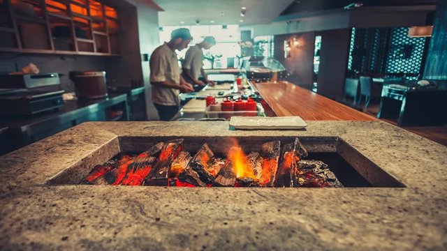 Open kitchen in modern restaurant interior. Bar counter made of natural stone with brazier closeup. Wood burn and the air melt from the heat. Blue color filter toning. 4k Slow Motion Parallax Effect
