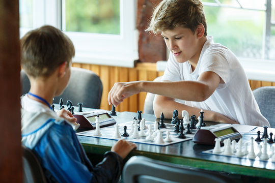 cute handsome boy in white tshirt plays chess with his rival in chess class. Education concept, intellectual game. Chess tournament, lesson, camp, training concept