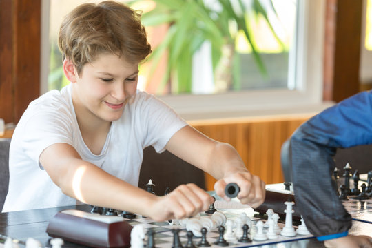 cute handsome boy in white tshirt plays chess with his rival in chess class. Education concept, intellectual game. Chess tournament, lesson, camp, training concept