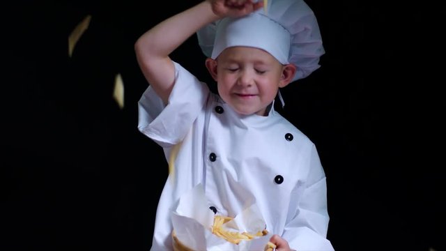 Cute boy toys with french fries, wearing chefs suit on the black background
