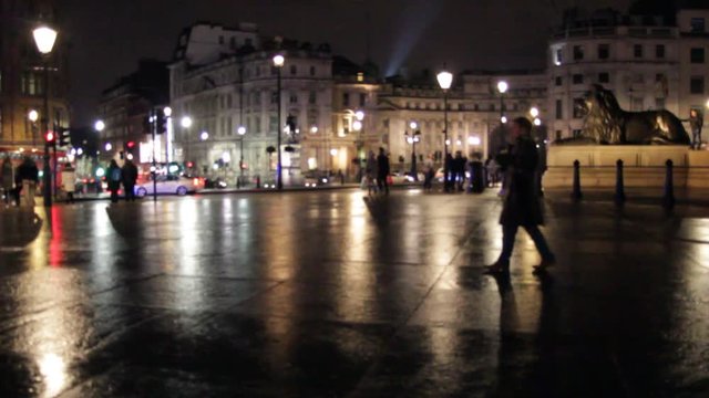 Trafalgar square at night red London bus and people walking around popular landmark on wet rainy evening 