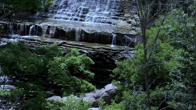 Waterfall panoramic landscape establishing shot. View of isolated and rock layered waterfall cascading into the forest floor. Hidden waterfall. 
