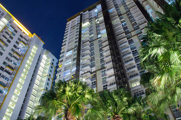 Fototapeta na wymiar Tropical palm trees and apartment windows at night. Highrise housing in large urban cities for rental and buyers housing mortgage concept.