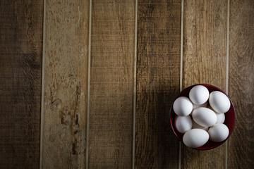 White chicken eggs, inside a bowl, on a wooden table. Top view.