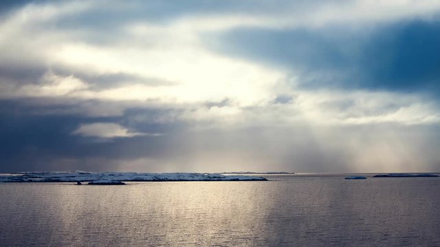 Antarctica. Cloudy dramatic sky with sun rays and calm ocean. Majestic winter landscape. Nature travel background. Ocean water waves movement, clouds in sky flow. 4K Slow Motion Time Lapse Parallax
