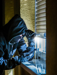 ein Einbrecher sieht nachts durch ein Fenster