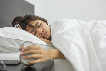 Asian woman sleeping in bed with retro alarm clock, young female lying in bedroom interior at night. Happy sleep concept